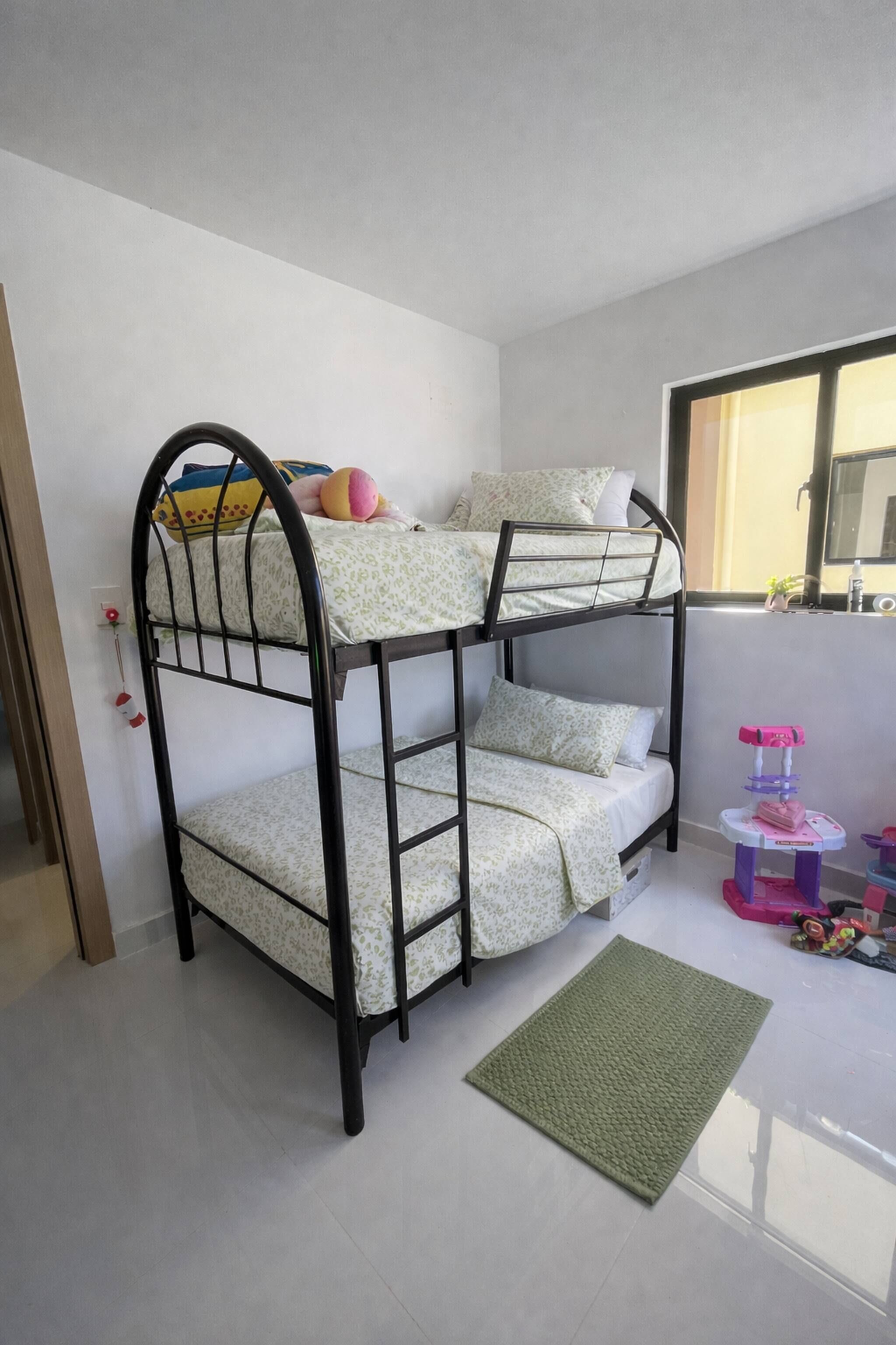 A bunk bed with a ladder, a green rug, and a small table with toys.