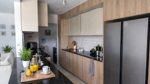 A modern kitchen with a black countertop, wooden cabinets, and a stainless steel refrigerator. - Mountain and Pool Modern Apartment (Santiago de los Caballeros)