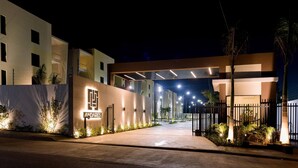 A modern hotel entrance with a well-lit facade, a gated driveway, and a covered walkway. - Mountain and Pool Modern Apartment (Santiago de los Caballeros)