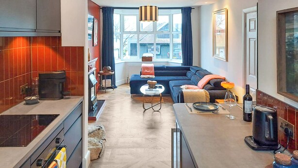 Een compacte leefruimte met een kitchenette, een bank, een eettafel en een groot raam.
