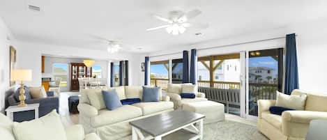A spacious living room with a large window, a ceiling fan, and a dining area visible through the glass doors.