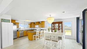 Uma cozinha moderna com armários de madeira, uma ilha central, cadeiras brancas e um lustre.