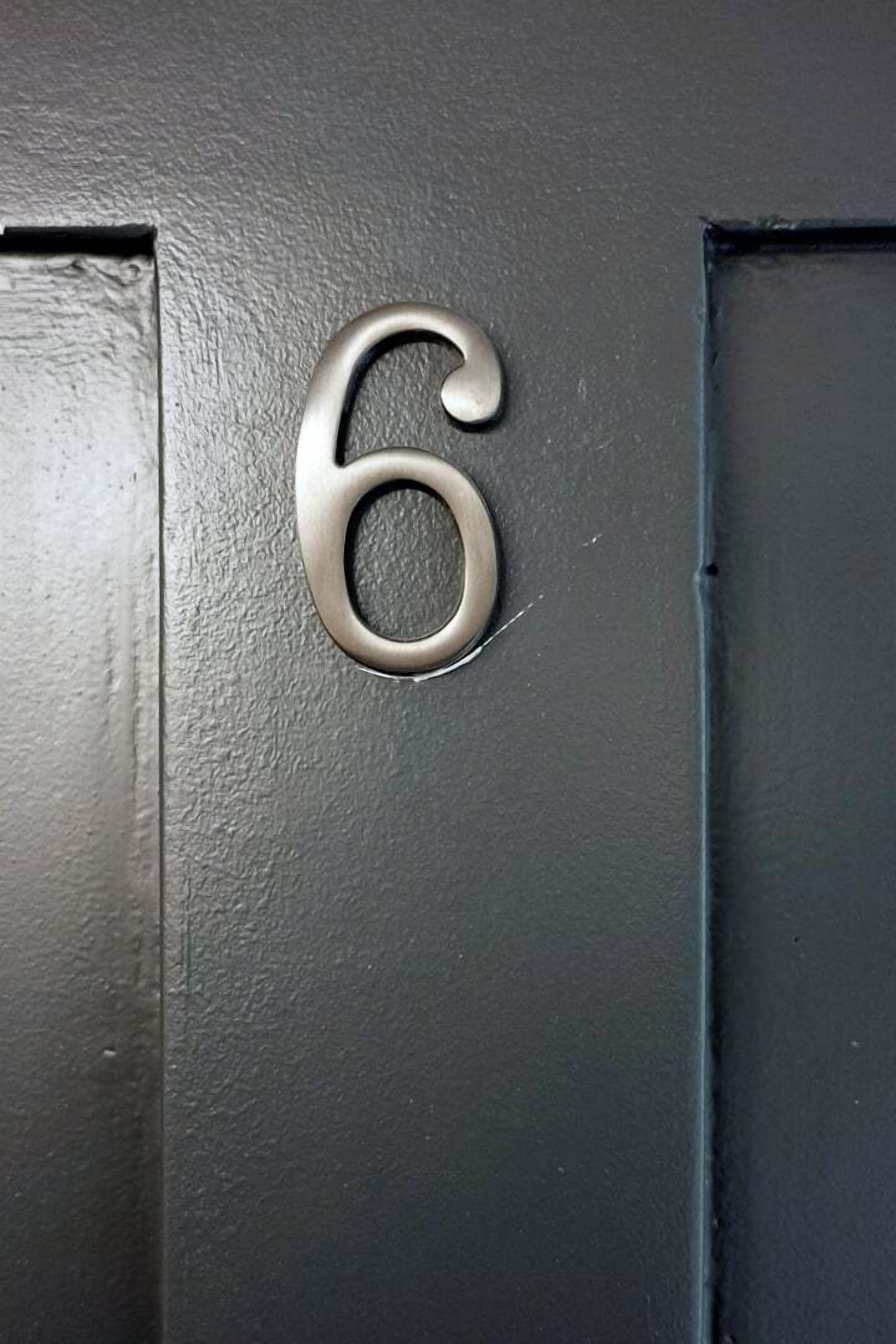 Primer plano del número '6' metálico sobre una puerta negra con textura.