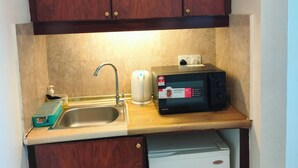Uma cozinha compacta com armários de madeira, pia de aço inoxidável, micro-ondas e uma geladeira pequena.