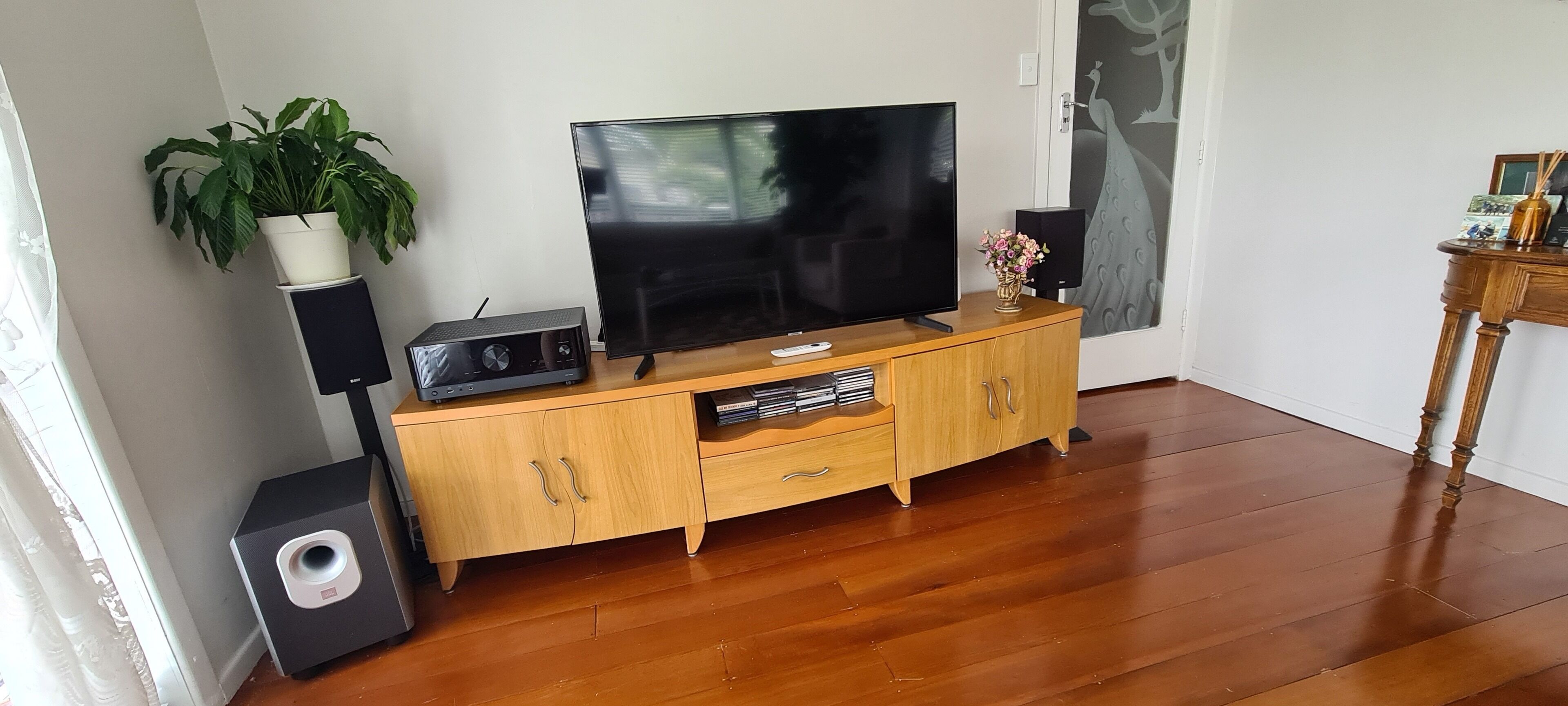 A living room with a wooden entertainment unit, a flat-screen TV, a speaker, and a potted plant.