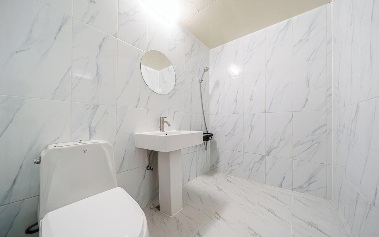 Une salle de bain avec des carreaux de marbre blanc, un lavabo blanc, des toilettes et une douche.