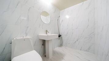 Un baño con baldosas de mármol blanco, un lavabo blanco, un inodoro y una ducha.
