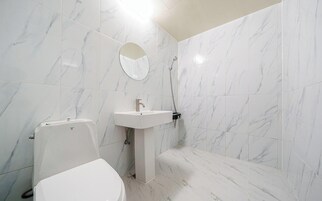 Un baño con baldosas de mármol blanco, un lavabo blanco, un inodoro y una ducha.