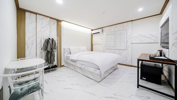 A modern hotel room with a marble-patterned bed, a small table with a TV, and a wardrobe with hanging clothes. - Hasen Wolgot Hotel (Siheung)
