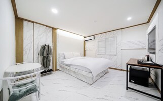 Una habitación de hotel moderna con una cama de diseño de mármol, una mesita con televisor y un armario con ropa colgada.