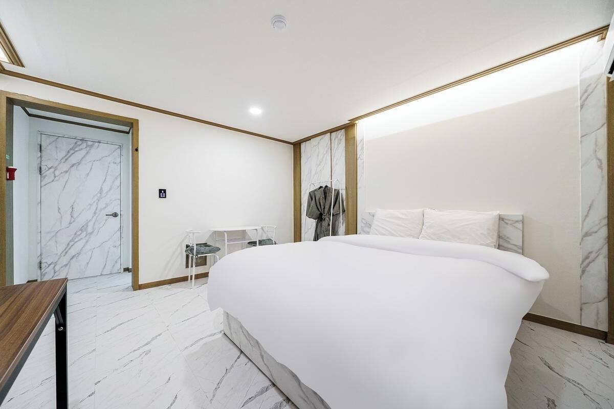 A hotel room with a large bed, a desk, a chair, and a wardrobe.