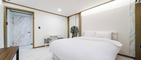 A hotel room with a large bed, a desk, a chair, and a wardrobe.