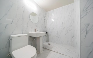 Un baño con inodoro, lavabo y zona de ducha, todo revestido de mármol blanco.