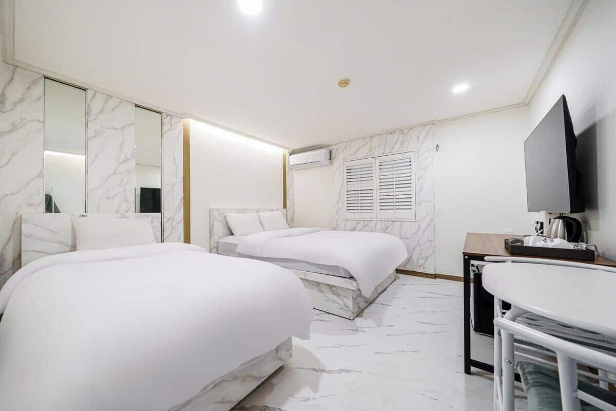 A hotel room with two beds, a TV, a desk, and a mirror.