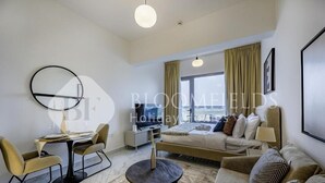 A modern hotel room with a sofa, a round coffee table, a TV, and a dining area with chairs and a table. - Bloomfileds Fabiouluxe Stu In Oasis (Abu Dhabi)