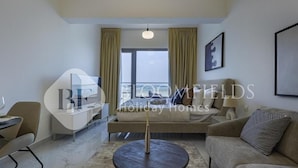 A modern hotel room with a sofa, a round coffee table, a TV, and a dining area. - Bloomfileds Fabiouluxe Stu In Oasis (Abu Dhabi)