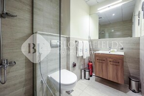 A modern bathroom with a glass shower enclosure, a white toilet, and a wooden vanity with a sink. - Bloomfileds Fabiouluxe Stu In Oasis (Abu Dhabi)