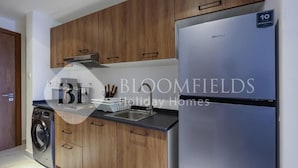 A modern kitchen with wooden cabinets, a stainless steel refrigerator, and a washing machine. - Bloomfileds Fabiouluxe Stu In Oasis (Abu Dhabi)