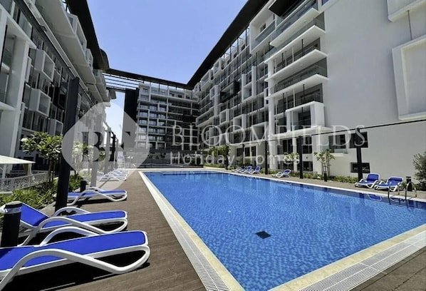 A modern hotel with a central swimming pool, sun loungers, and a clear sky. - Bloomfileds Fabiouluxe Stu In Oasis (Abu Dhabi)