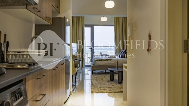 A modern kitchen with wooden cabinets, a built-in oven, and a dining area with a sofa and a small table. - Bloomfileds Fabiouluxe Stu In Oasis (Abu Dhabi)