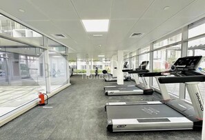 A gym with treadmills, a fire extinguisher, and large windows. - Bloomfileds Fabiouluxe Stu In Oasis (Abu Dhabi)