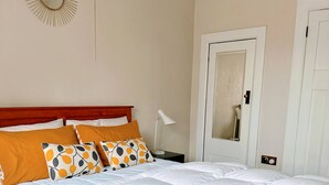 Ein ordentlich bezogenes Bett mit weißer und orangefarbener Bettwäsche, einem Holz-Kopfende und einer Nachttischlampe.