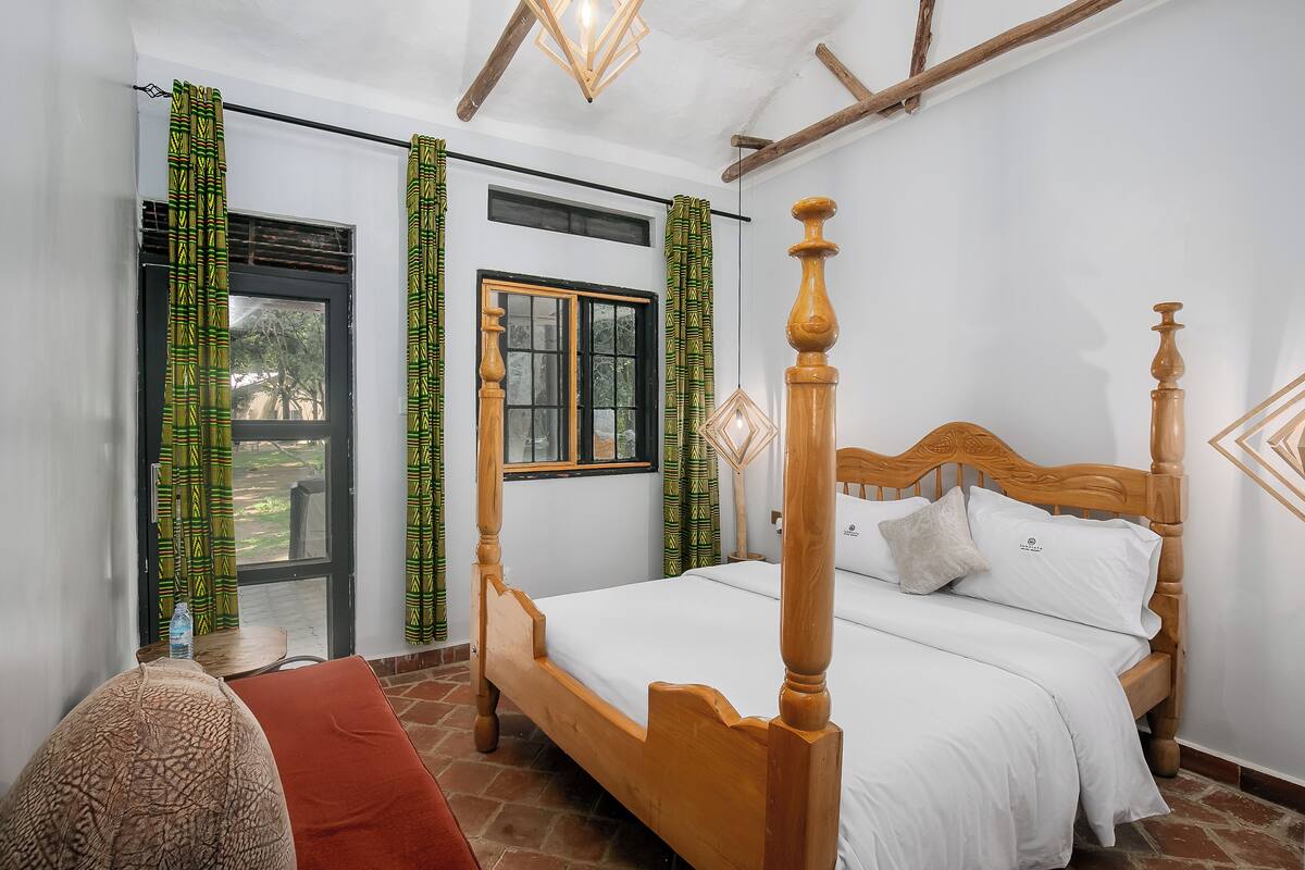 A four-poster bed with white linens, a wooden headboard, and a window with a black frame.