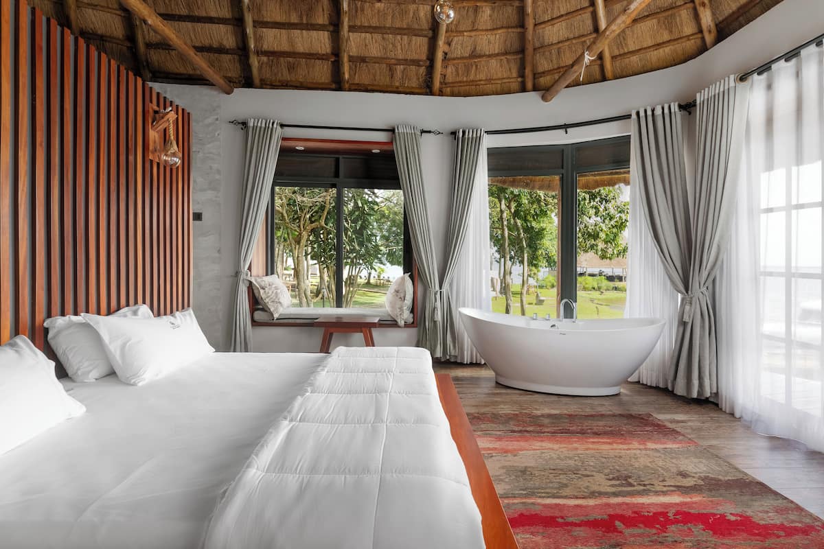 A bedroom with a large bed, a bathtub, and a view of greenery.
