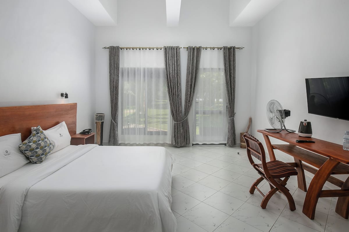 A hotel room with a bed, a desk with a chair, a television, and a window with curtains.