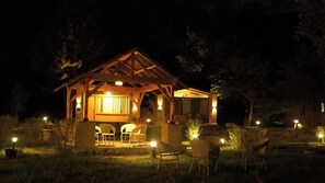 A wooden gazebo with a covered seating area and tables, surrounded by chairs, under night lighting. - Misty Hills Cabins Nubra (Hunder)