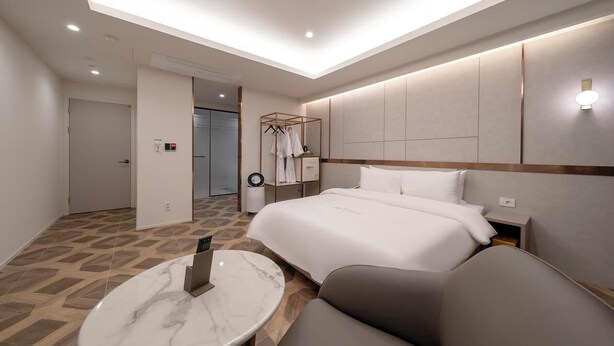A modern hotel room with a large bed, a seating area with a marble table, and a walk-in closet with clothing. - Gwangmyeong Hotel Levento (Gwangmyeong)
