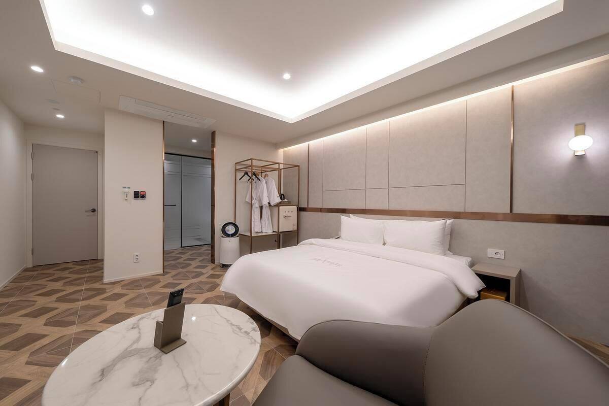 Een moderne hotelkamer met een groot bed, een zithoek met een marmeren tafel, en een inloopkast met kleding.