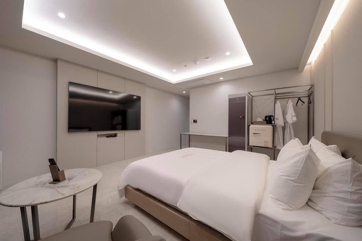 Een moderne hotelkamer met een groot bed, een flatscreen televisie aan de muur, een klein tafeltje met een telefoon en een douche met een handdoekhouder.