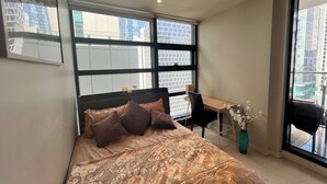 A bedroom with a bed, a desk, and a chair. There are large windows with a city view. - Room-room in Melbourne CBD (Melbourne)