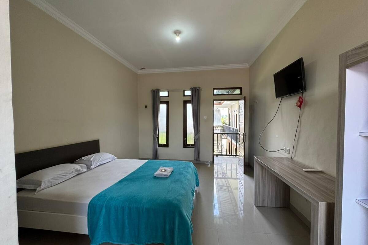 A hotel room with a bed, a desk, a TV, and a balcony.