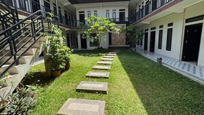 Un cortile con un percorso centrale, piante in vaso e una scala a sinistra.