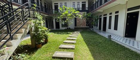 A courtyard with a central pathway, potted plants, and a staircase on the left.