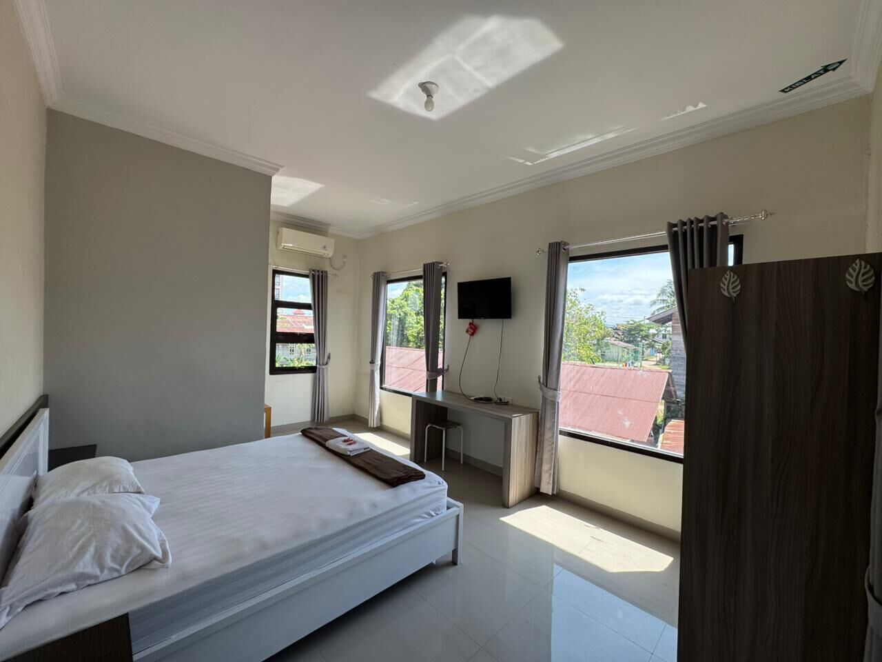 A bedroom with a bed, a desk, a chair, a TV, and a view of the outside.