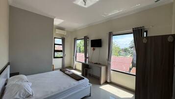 A bedroom with a bed, a desk, a chair, a TV, and a view of the outside.