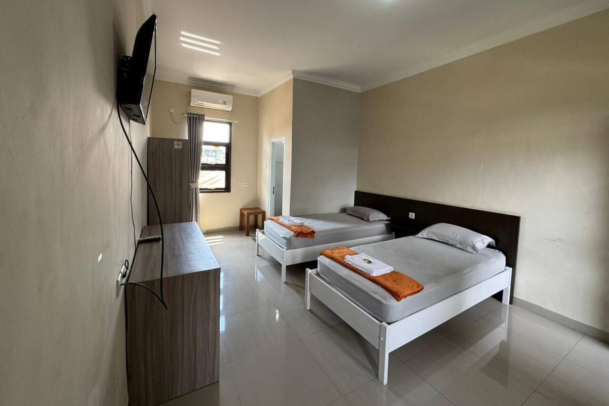 A hotel room with two beds, a desk, and a TV mounted on the wall.