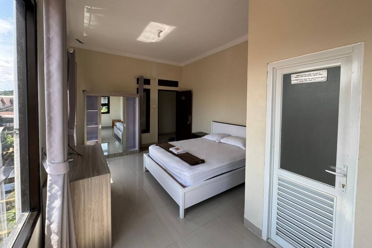 A hotel room with a bed, a window with curtains, a door with a sign, and a view of the outside.