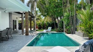Ein Pool mit Liegestühlen, umgeben von Palmen und Grünpflanzen.