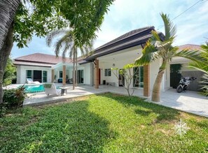 Ein modernes Haus mit Swimmingpool, überdachter Terrasse und gepflegtem Rasen.