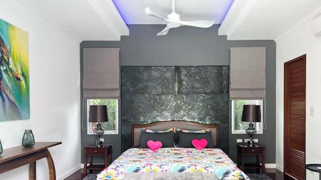 A bedroom with a large bed, two bedside tables with lamps, a ceiling fan, and a large abstract painting on the wall.
