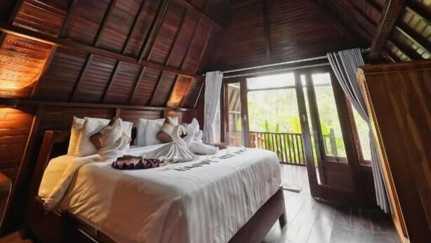 Un dormitorio con techo de madera, una cama grande y vistas al verdor exterior.