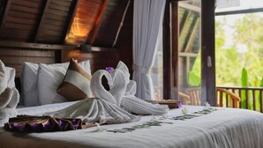 Habitación de hotel con cama, almohadas, una decoración de toallas con forma de cisne y vistas al exterior con vegetación.
