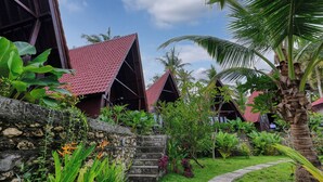 Un resort tropical con edificios de madera, un muro de piedra y exuberante vegetación.