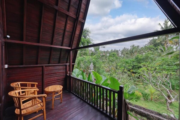 A wooden deck with two chairs and a table, overlooking a lush garden with various plants and trees.