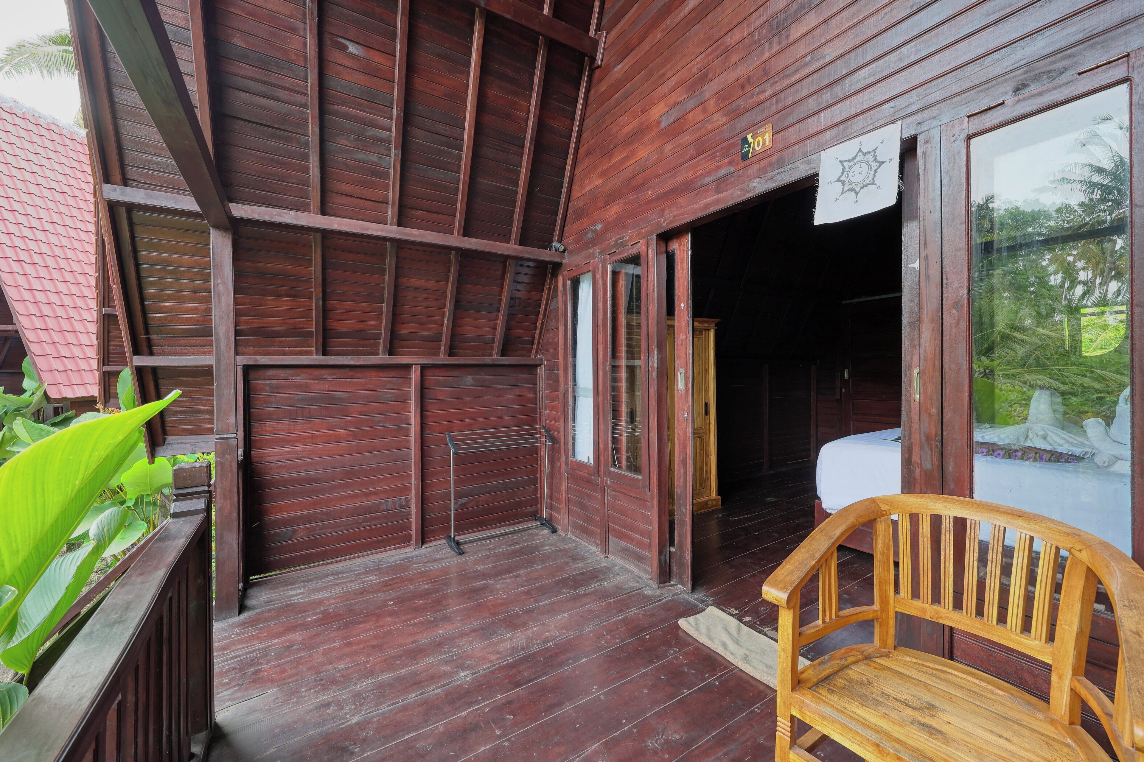 A wooden building with a porch, a bench, and a bed visible inside.