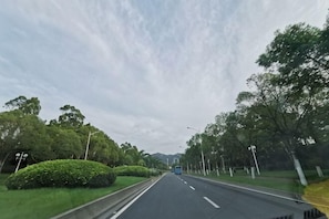 A road with a blue bus in the distance, surrounded by trees and greenery. - Xiamen qing cha Hotel (Xiamen)
